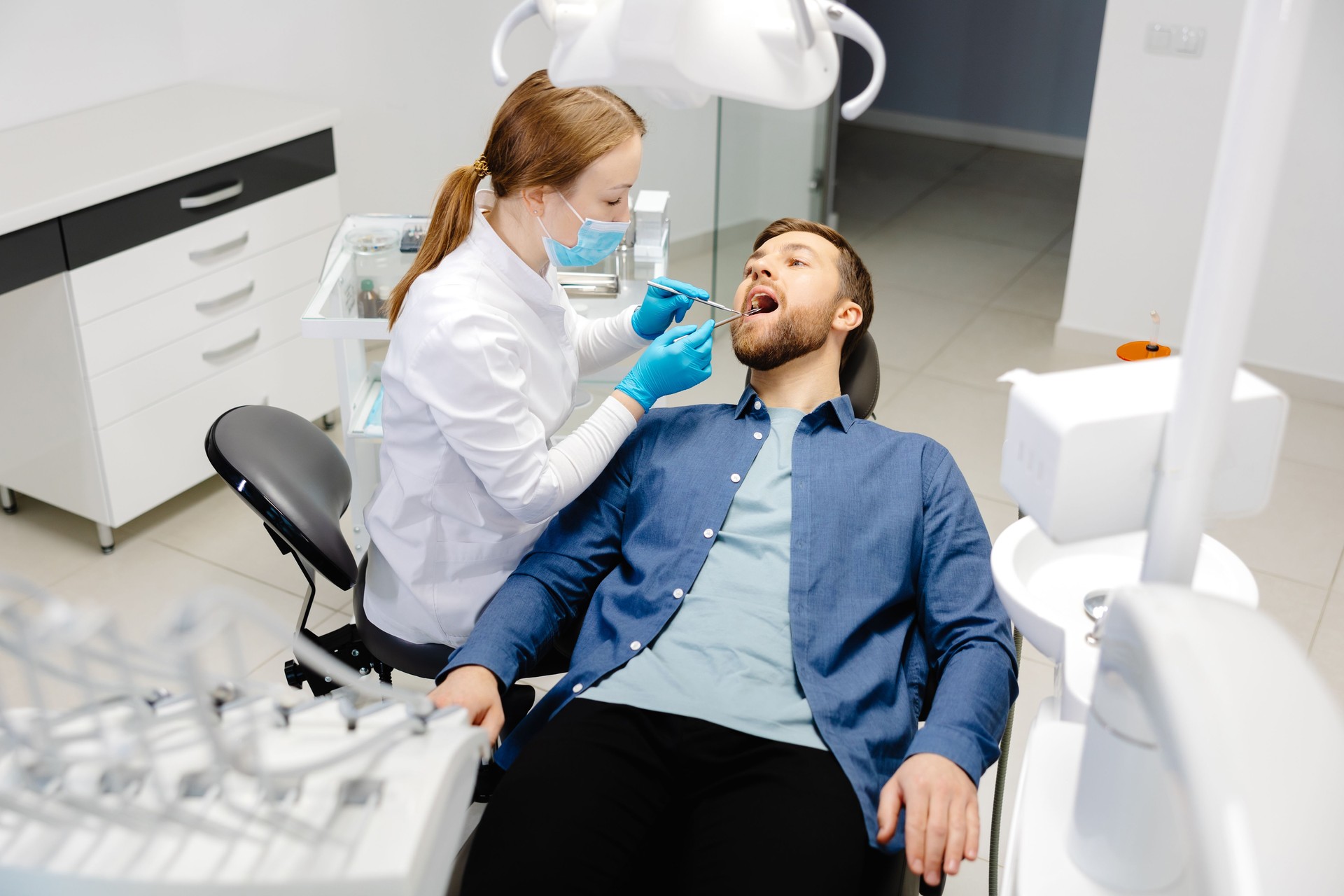 A handsome man is sitting in a chair at a woman's appointment at the dentist's office